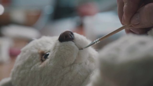 A thin brush in the hands of the artist to create soft toys. Fine brush for drawing: the mouth of a soft toy. Teddy bear in vintage style: the process of creation. Handmade toys.