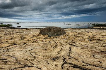 Fototapeta na wymiar Dry crannied ground and cloudy sky on the beach. Big stone in the center. Baltic Sea coastline, Estonia.