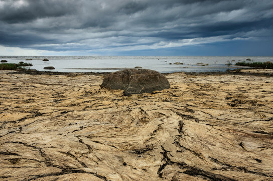 Dry crannied ground and cloudy sky on the beach. Big stone in the center. Baltic Sea coastline, Estonia.