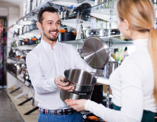 Fototapeta na wymiar Male shop assistant helping customer to choose saucepan