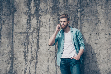 Stylish young red bearded man in casual jeans outfit is talking on his phone outside. He looks fashionable and mature