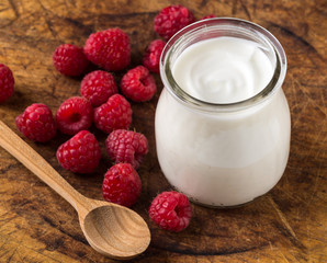 White yogurt with raspberries in glass bowl on natural wooden table.