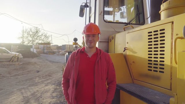 Portrait of a tractor driver in orange helmet near a tractor at construction site