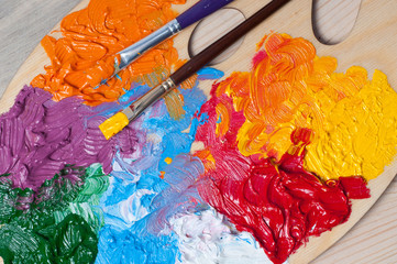 Palette of the artist with multi-colored oil paints and brushes on a wooden background
