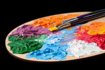 Palette of the artist with multi-colored oil paints and brushes on a black background