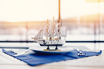 miniature sailing ship made of wood stands in a plate in the restaurant, behind it there is a...