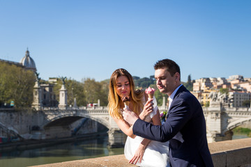 Fototapeta premium Bride and groom wedding poses with ice-cream in Vatican on the bank of the river Tiber, Rome, Italy