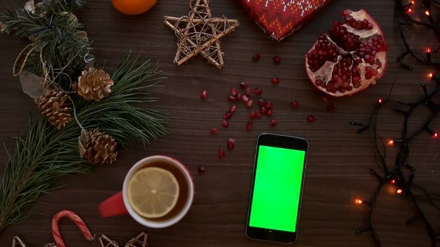 Top view man hand using smart phone with green screen. Finger tapping on touchscreen. Christmas details on wooden table background. Chroma key