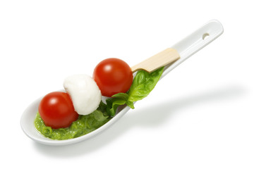 Caprese salad on sticks with pesto sauce on a ceramic spoon on a white background
