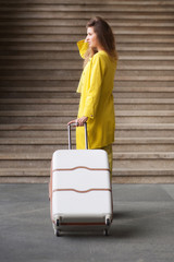 Young woman dressed in yellow suit holding suitcase and standing in front of stairs on railway station