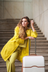 Young woman touching her hair, leans on the suitcase handle and looking at something