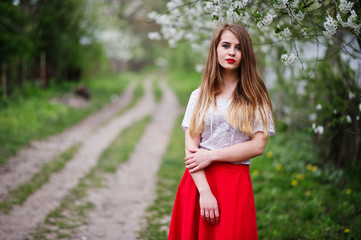 Portrait of beautiful girl with red lips at spring blossom garden, wear on red dress and white blouse.