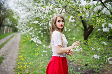 Portrait of beautiful girl with red lips at spring blossom garden, wear on red dress and white blouse.