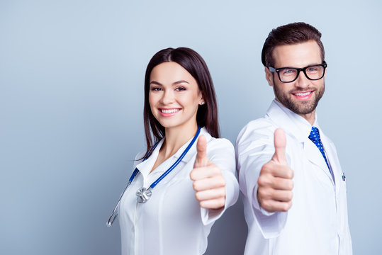 Two successful doctors in uniform together showing thumbs-up on gray background