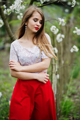 Portrait of beautiful girl with red lips at spring blossom garden, wear on red dress and white blouse.