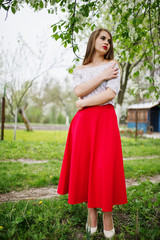 Portrait of beautiful girl with red lips at spring blossom garden, wear on red dress and white blouse.
