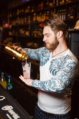 Bearded barman prepares a cocktail seriously