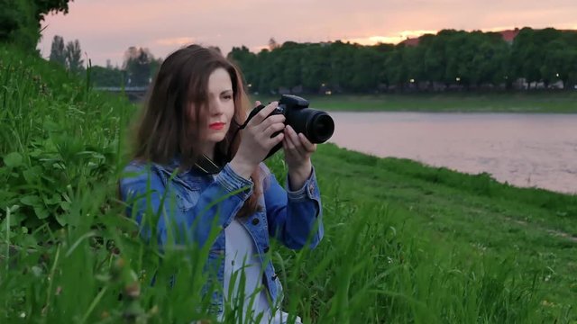 Beautiful girl tourist shoots a video with a professional camera on the banks of the river in windy weather