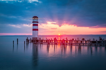 Lakeside sunset scenery with lighthouse on a peer - obrazy, fototapety, plakaty