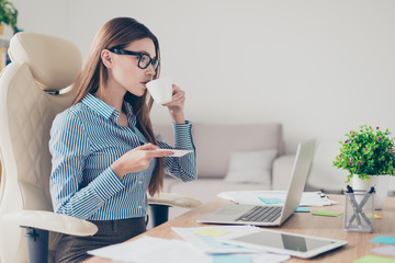 Successful relaxed economist is resting at her work place and drinks coffee while reading her mail...