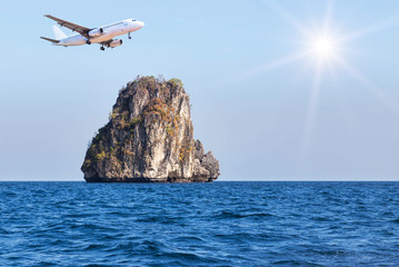 Fototapeta na wymiar passenger airplane flying above small limestone island in tropical andaman sea with sunlight. travel destinations concept