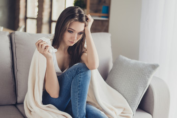 Young worried depressed woman sitting on sofa with blanket on her shoulders