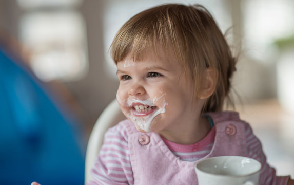 Close up portrait of little girl with messy face drinking yogurt