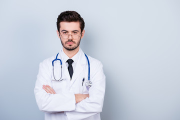 Fototapeta premium Portrait of concentrated minded doctor in white coat standing with crossed hands against gray background