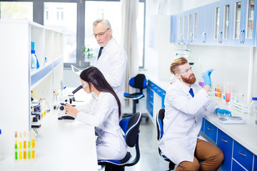 Fototapeta premium Teambuilding concept. Three workers of laboratory are ckecking the analysis. They look stylish, wearing labcoats. The lab is bright white and blue