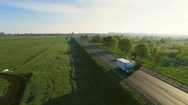 4K aerial footage of cars riding on a road between green fields in the sun rise