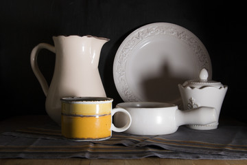 Dark country style milk pitcher, creamer and old vintage mug on black background
