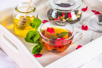 Flower tea in a cup, a jar of honey, tea in a jar, on a white tray in bed.