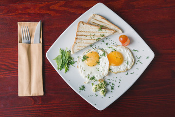 Breakfast in restaurant - fried eggs on white plate with green and tomato cherry