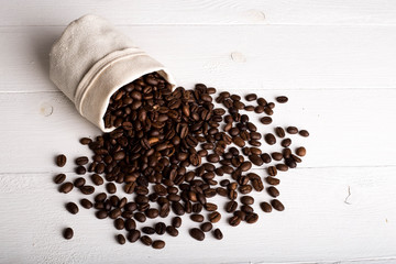 Coffee beans fallen out of a white jute bag located on wooden table. Top view. Copy place. Selective focus. Macro close-up for design work.