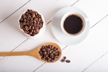 Cup of coffee, coffee beans in the bag, wooden spoon on a wooden white background table. Top view. Place for text or inscription.de view. Place for text or inscription.