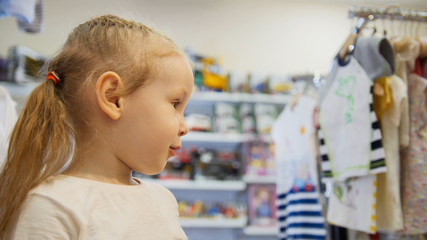 Obraz premium Cute blonde baby girl in child dress store