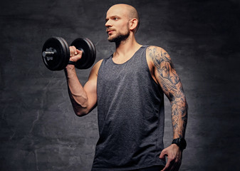 Fototapeta na wymiar Sporty shaved head tattooed male doing biceps workout with dumbbell.