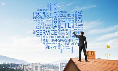 Young businessman standing on house roof and writing leadership skill concept. Mixed media