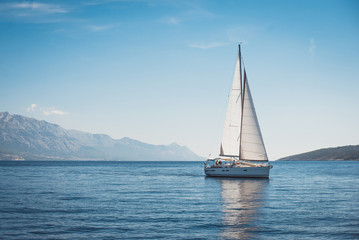 Sailing yacht in the sea against the backdrop of mountains - obrazy, fototapety, plakaty