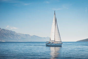 Sailing yacht in the sea against the backdrop of mountains - obrazy, fototapety, plakaty