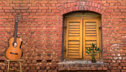 Music background content with acoustic guitar against a red brick wall with a vintage window.