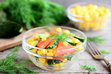 Summer salad with cucumbers, tomatoes and corn. Bright, easy and yummy salad in a bowl. Healthy vitamin vegetable food. Fork, cucumber, dill on a wooden table. Rustic style