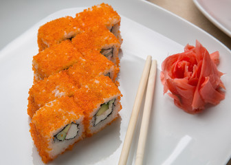 California rolls on a white plate next to the sticks and ginger