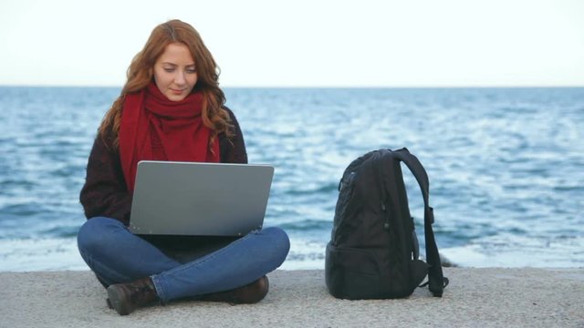 Young woman with laptop sitting on the beach typing and browsing the web