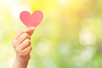 paper heart in hand on abstract nature background.