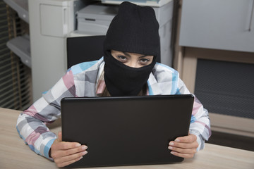 Hacker looks from behind a computer, looking at you