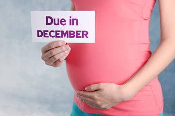Pregnant woman holding paper with words DUE IN DECEMBER