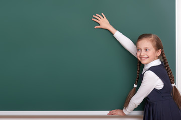 elementary school girl put hands on chalkboard background and show blank space, dressed in classic black suit, group pupil, education concept