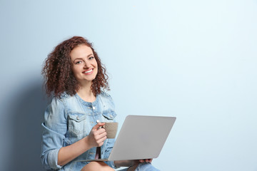 Beautiful young woman using laptop on light wall background