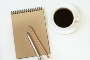 Workspace with notebook of craft paper, pencil, cup of coffee on white background. Image with copy space for your text.